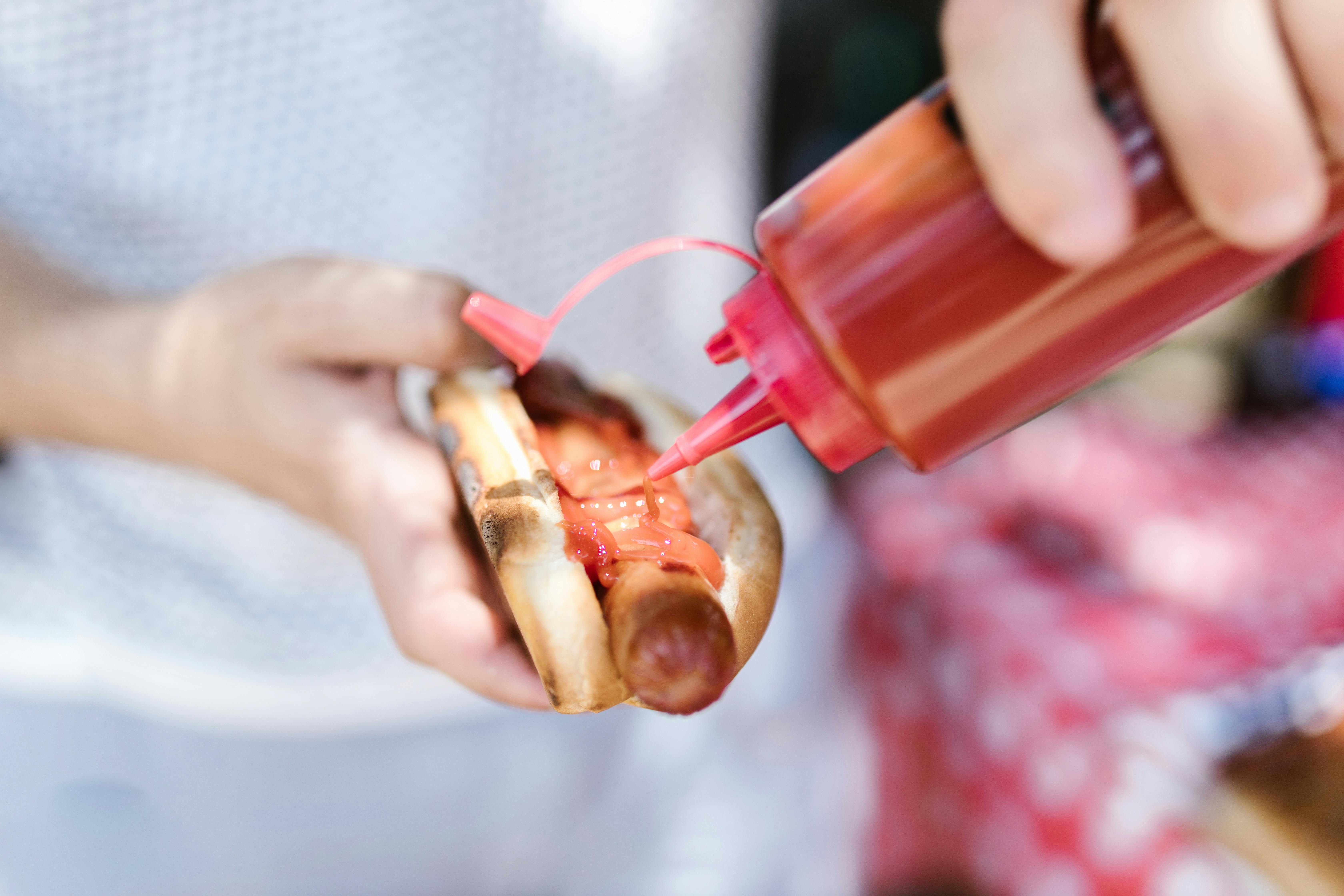 A person putting ketchup on a hotdog | Source: Pexels