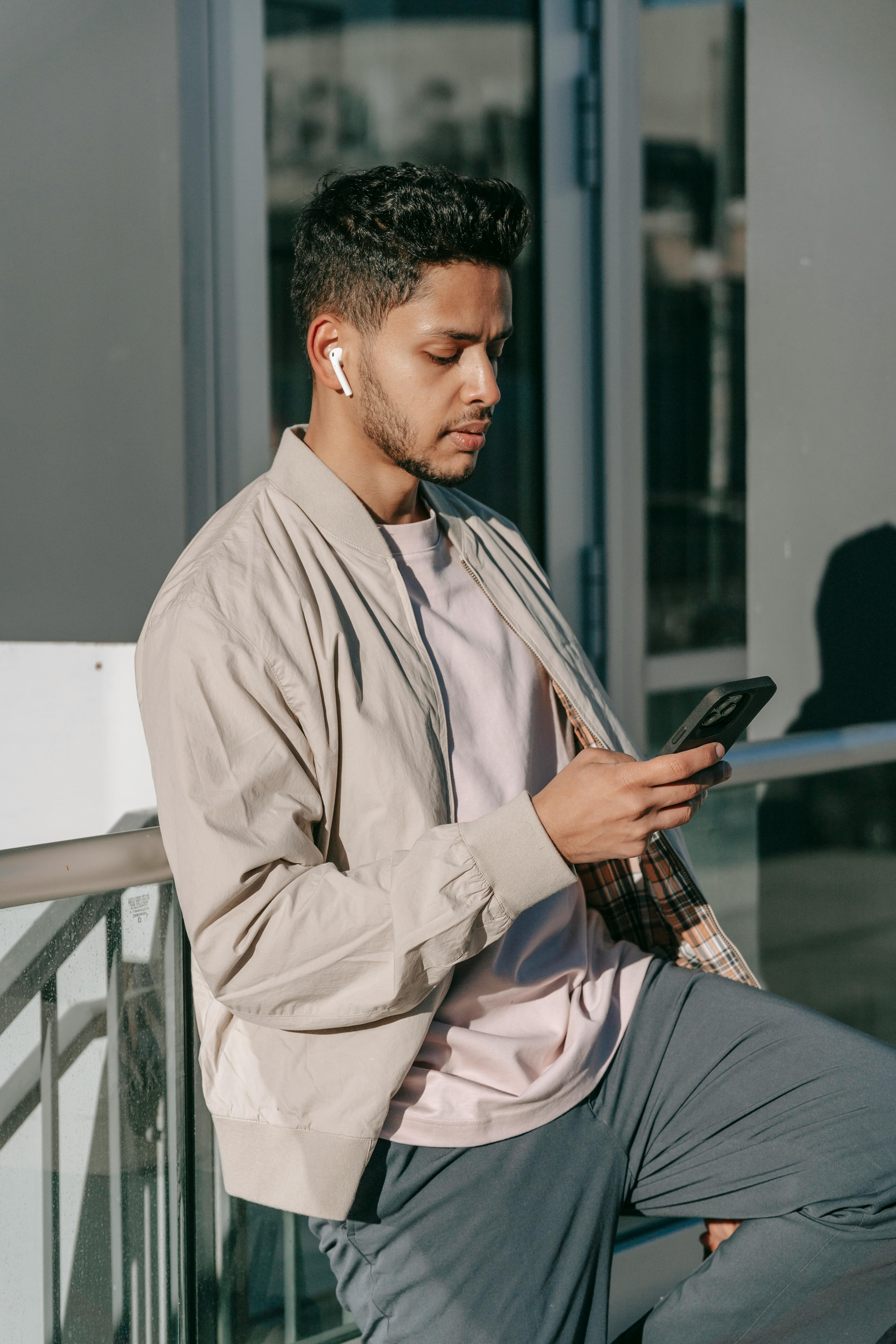 A displeased-looking man wearing ear pods while using his phone | Source: Pexels